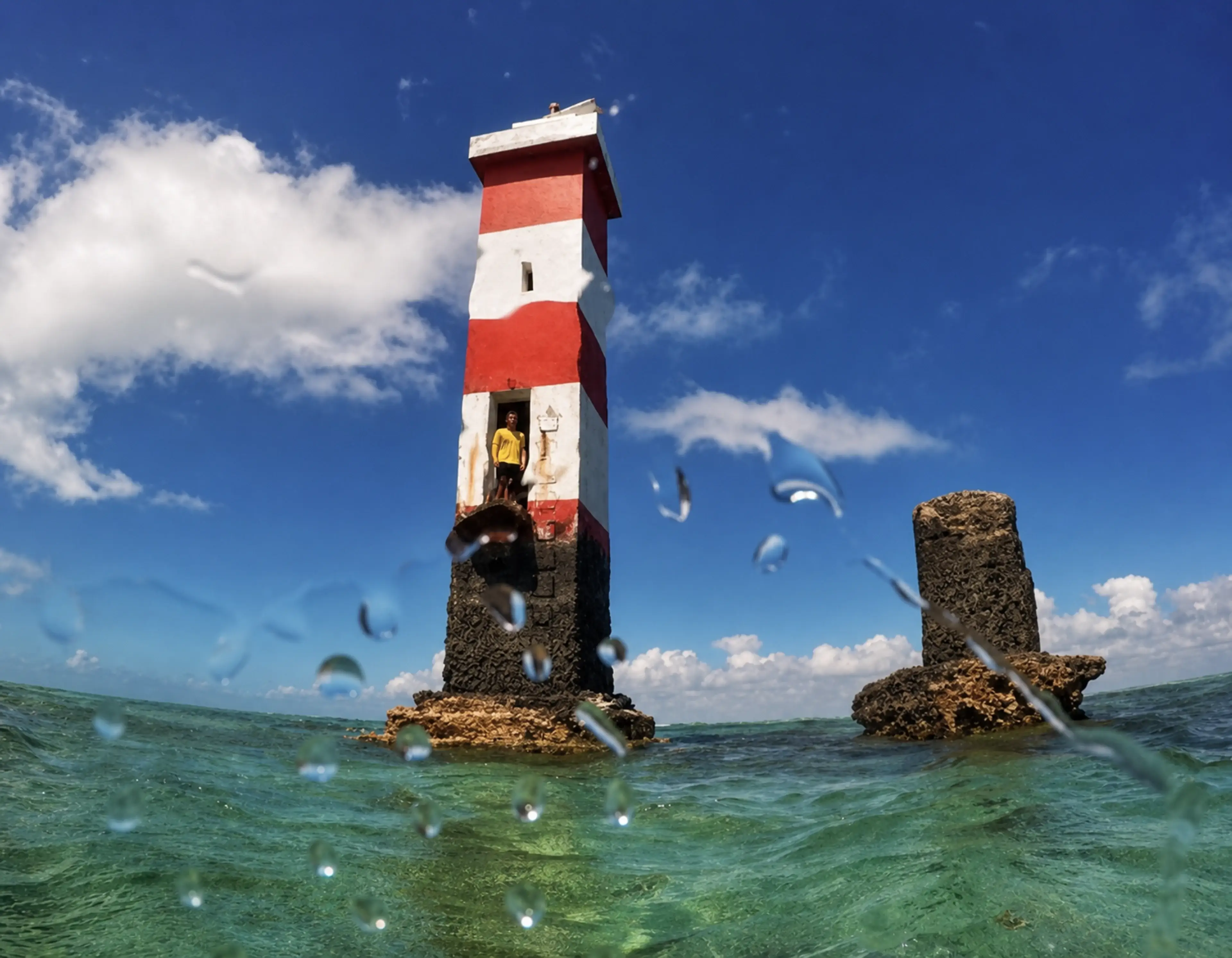 Farol listrado em vermelho e branco cercado pelo mar